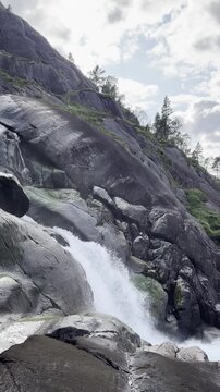 A cinematic aerial view of Langfossen Waterfall in Norway. The camera follows the cascading water downstream, revealing the landscape before ending with a breathtaking view of &Aring;krafjorden fjod.