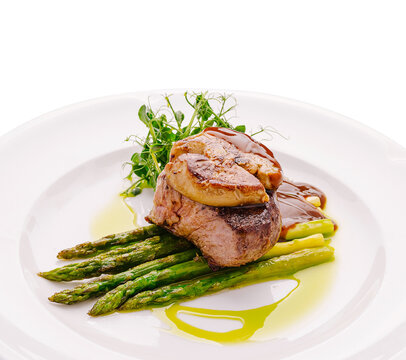 Exquisite Tournedos Rossini steak rests on fresh green asparagus. Luxury restaurant gourmet meal is decorated with rich brown sauce.