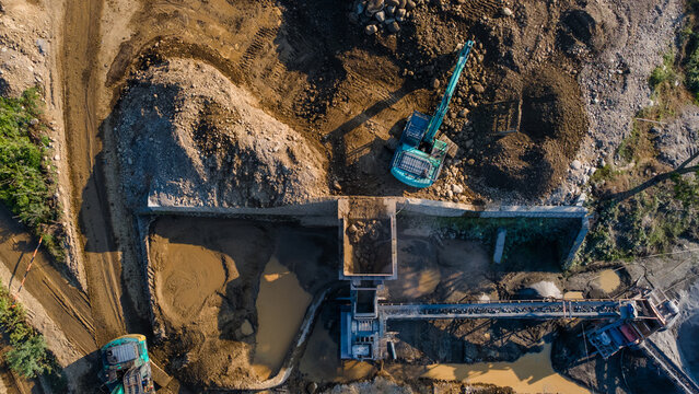 Aerial View of Excavator Processing Ore Near Rock Crusher Facility in Mining Quarry, Construction and mining site view from above.