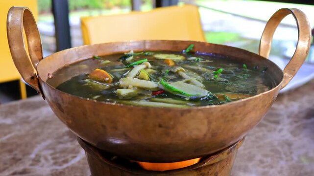 Simmering northeastern Thai mixed mushroom soup served in a traditional hot brass pot