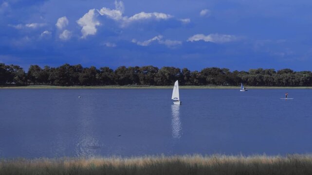 People enjoying watersports with sailboats and SUP boards on a vibrant blue lake under a clear sky