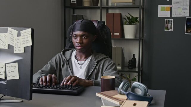 Young African American programmer typing on keyboard and looking at computer screen in office. Footage for commercial videos about software development, IT startups, and remote tech jobs