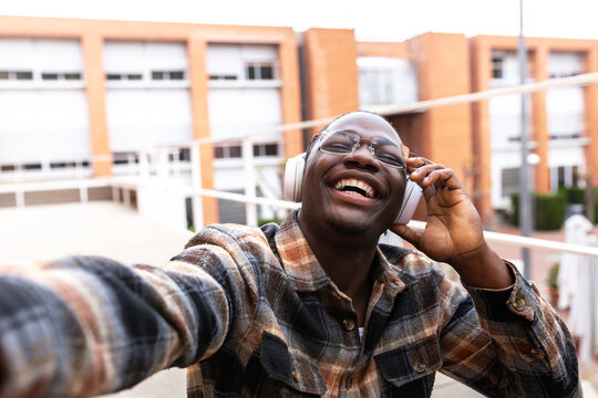 Happy student taking a selfie while listening to music with headphones outdoors