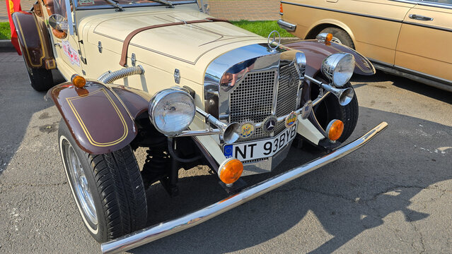 Piatra Neamt, Romania - June 7, 2025: Front view of a beige and brown 1929 Mercedes-Benz SSK Gazelle roadster replica with a prominent chrome grille, emblem, and headlights.
