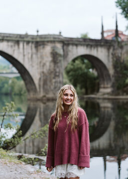 Happy young woman standing by a river with a stone bridge