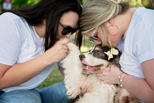 Two women cuddling and kissing a beloved senior spaniel outdoors