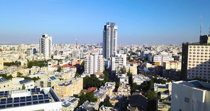 Drone shot descending over the urban skyline of Ramat Gan in central Israel. The aerial view reveals a dense metropolitan landscape of residential buildings, office towers, and modern architecture str