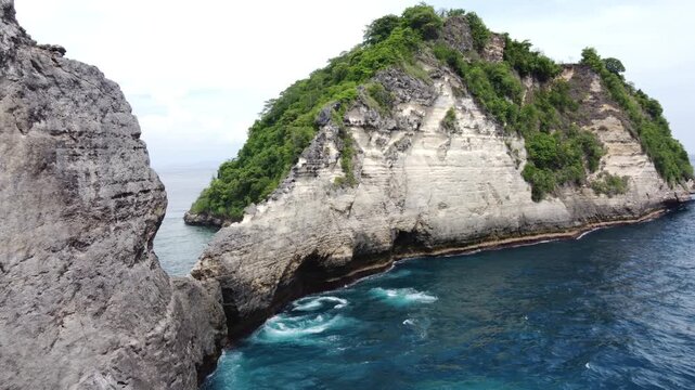 Aerial drone view of dramatic limestone cliffs and clear blue ocean at Atuh Beach, Nusa Penida, Bali. Tropical coastline with rugged rock formations and lush greenery