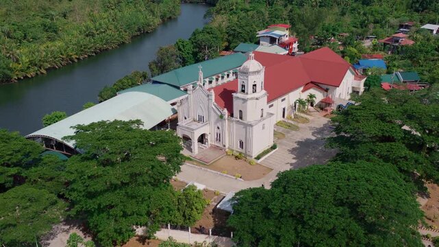Aerial angled approach of Saint Paul the Apostle Parish Church beside river in Inabanga Bohol, Philippines