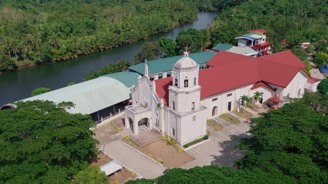 Aerial close orbit of Saint Paul the Apostle Parish Church beside river and tropical forest, drone, Bohol Philippines