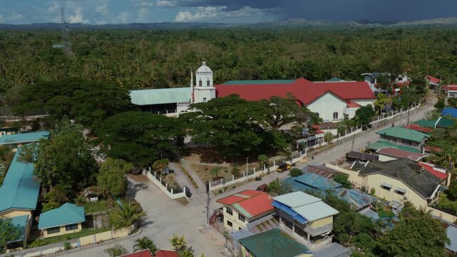 Aerial approach of Saint Paul the Apostle Parish Church and Inabanga town surrounded by tropical greenery, Bohol Philippines