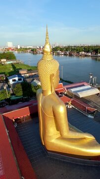 Drone view of Wat Bang Chak temple near Koh Kret Island, featuring a giant golden Buddha statue beside the Chao Phraya River in Nonthaburi, Thailand.
