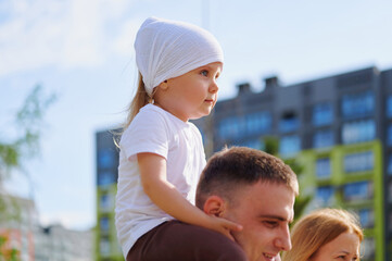 Cute little girl enjoying a piggyback ride on her father's shoulders outdoors, exploring the city on a sunny day. © khmelev