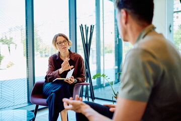 Female professional giving guidance and support to a man during a therapy session in a modern office setup
