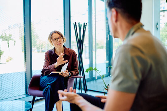 Female professional giving guidance and support to a man during a therapy session in a modern office setup