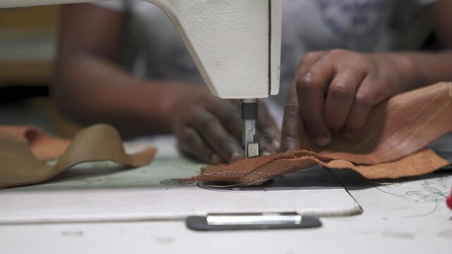Close-up of hands expertly guiding leather under a sewing machine needle, capturing the precision of leather crafting. Suitable for artisan craft demonstrations or educational content.