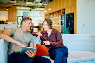 Naklejka premium Two business colleagues sitting on a couch, discussing work and sharing ideas while using a digital tablet in a casual office setting