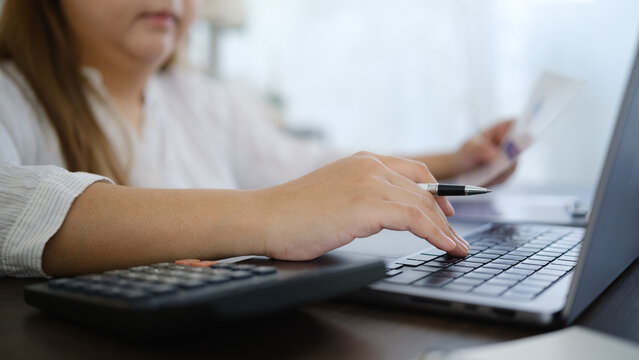 Woman using a laptop and calculator while reviewing bills at home, representing online banking, budgeting, and personal finance planning.