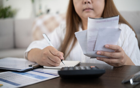 Close up of a woman calculating expenses while holding receipts, representing budgeting, personal finance, and household bill payment.
