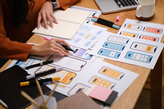 UX designer working on mobile app wireframes with markers, notebooks, and printed interface layouts on a desk.