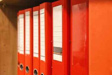 Red ring binders on wooden shelf closeup in corporate office. Concept: tax audit © Marya