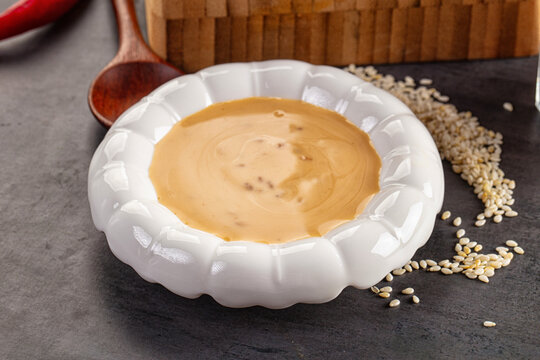 sesame tahini paste in white ceramic bowl with wooden spoon