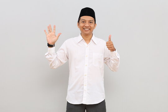 Asian Muslim man smiling while raising six fingers, isolated on gray background.