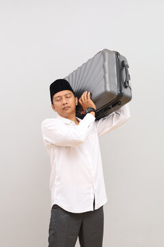 An excited Asian Muslim man stands with his suitcase on his shoulder and his eyes closed, making his mudik or homecoming journey to celebrate Eid al-Fitr in the month of Ramadan.
