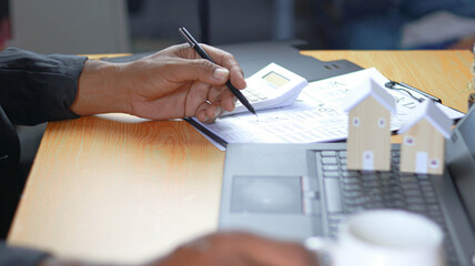 Business professional analyzing real estate and mortgage documents at office desk with calculator, laptop and house models. Concept of home loan approval, property investment, financial planning   © Siwaporn
