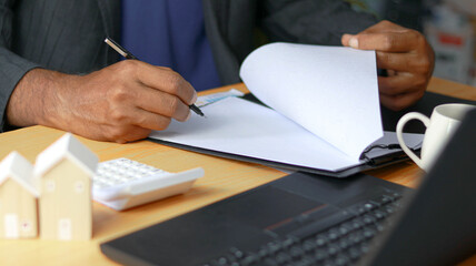 Business professional reviewing and signing financial documents at office desk with calculator,...