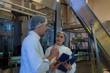 Naklejka premium Food and Beverage Industry Workers in White Lab Coats and Hairnets Using Digital Tablets to Monitor and Inspect Automated Wine Bottling Production Line in Modern Winery Manufacturing Facility