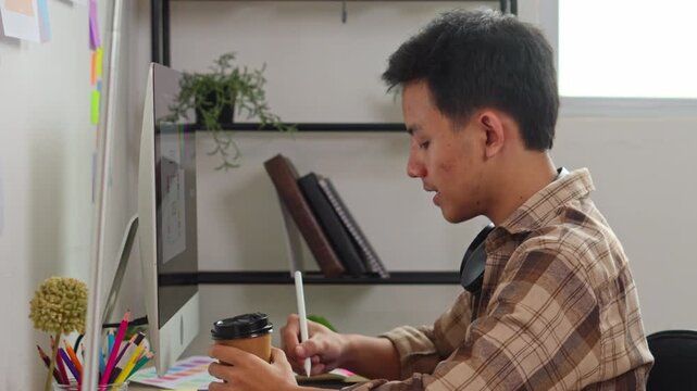 Professional graphic designer working on computer while drinking coffee in bright