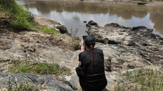 Behind view of a woman capturing landscape and animal pics at Masai Mara river