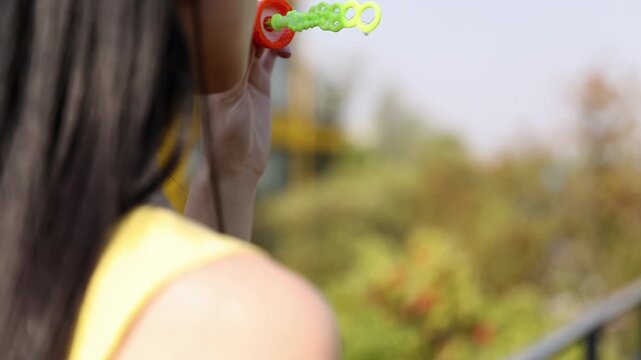 Trendy fashionable young girl playing outside blowing soap bubbles in the park, smiling, laughing and happy in summer outdoors