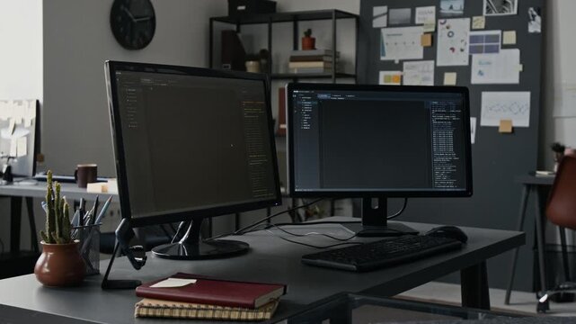 Dual computer monitors displaying software programming code sitting on desk in empty IT office. Footage for tech startups, software development agencies, and online coding schools