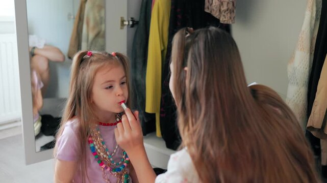Happy tween girl putting makeup on younger sister smiling in bedroom.
