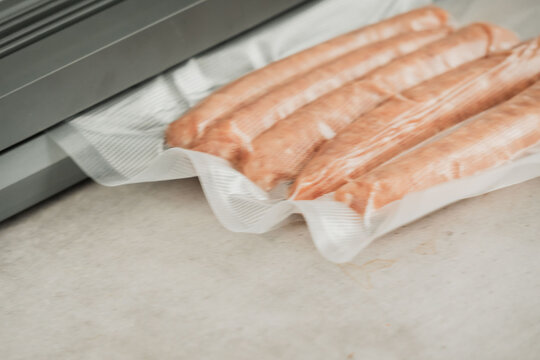 Fresh raw sausages in vacuum tray on countertop near packaging machine