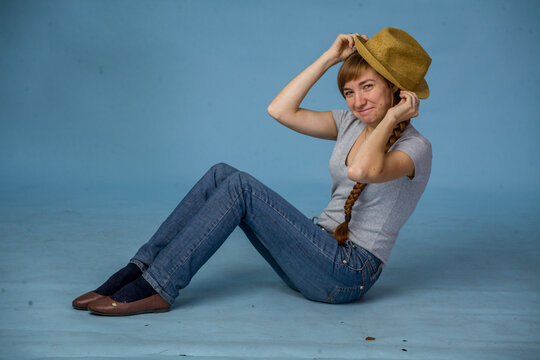 Young woman playfully wearing a hat while sitting on blue background  