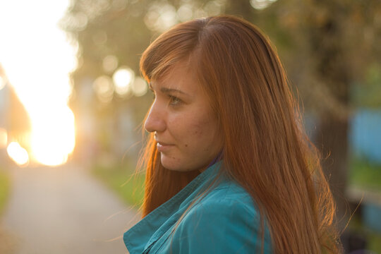 Woman with long red hair looking thoughtfully outdoors at sunset  