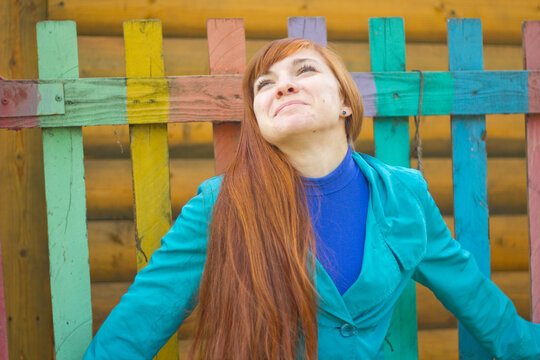 Young woman smiling with arms raised in front of colorful fence  
