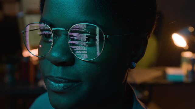 Extreme close-up view of African American woman programmer wearing glasses reflecting computer code, working on software development. Footage for technology, cybersecurity, or IT startup marketing