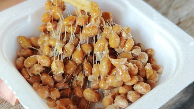 Chopsticks lifting sticky fermented natto soybeans.