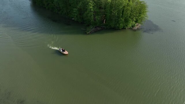 Drone video capturing a small motorboat sailing on the river estuary next to a green island and pedestrian bridge in the coastal resort of Anaklia, Georgia, with the sun reflecting on the water.