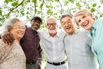 Diverse group of smiling elderly friends posing outdoors under trees.