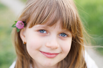 Fototapeta premium Smiling Young Girl Standing in Green Meadow with Wildflower in Hair