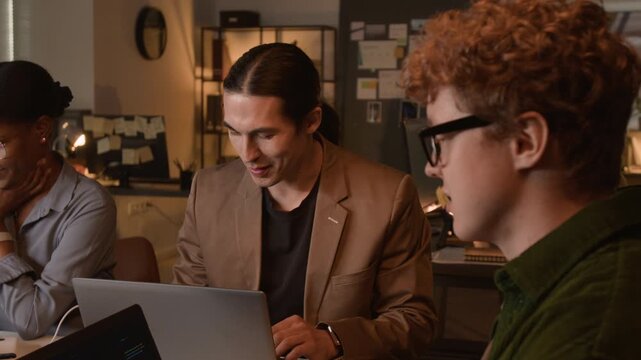 Multiethnic young programmers working on laptops in office, discussing code and smiling. Footage for software development marketing and IT recruitment campaigns