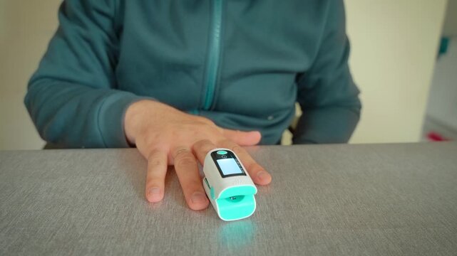 Pulse oximeter oxygen saturation measurement on finger at home. Adult man checking blood oxygen level and pulse rate during respiratory illness recovery. Health monitoring for flu coronavirus