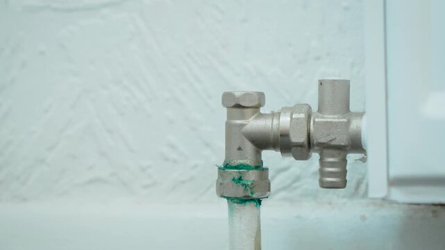 Corroded radiator valve with oxidized mineral deposits on central heating pipe. Close up heating system fitting showing green corrosion stains and metal deterioration. Plumbing maintenance, household