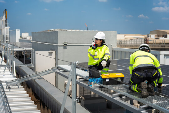 Technicians installing solar panels on commercial building rooftop, Team of engineers working on solar photovoltaic cell installation at industrial facility
