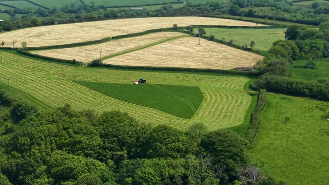 Tractor towing heavy-duty grass cutter efficiently mowing green field in English countryside creating elegant shape. Agricultural industries, commercial landscaping, rural lifestyle. 4K.